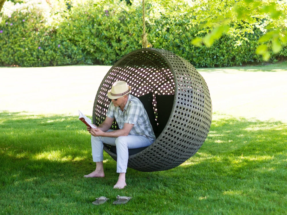 Alexander Rose Monte Carlo Hanging Chair Hanging From a Tree Man Sat Reading Luxury Rattan Garden Furniture
