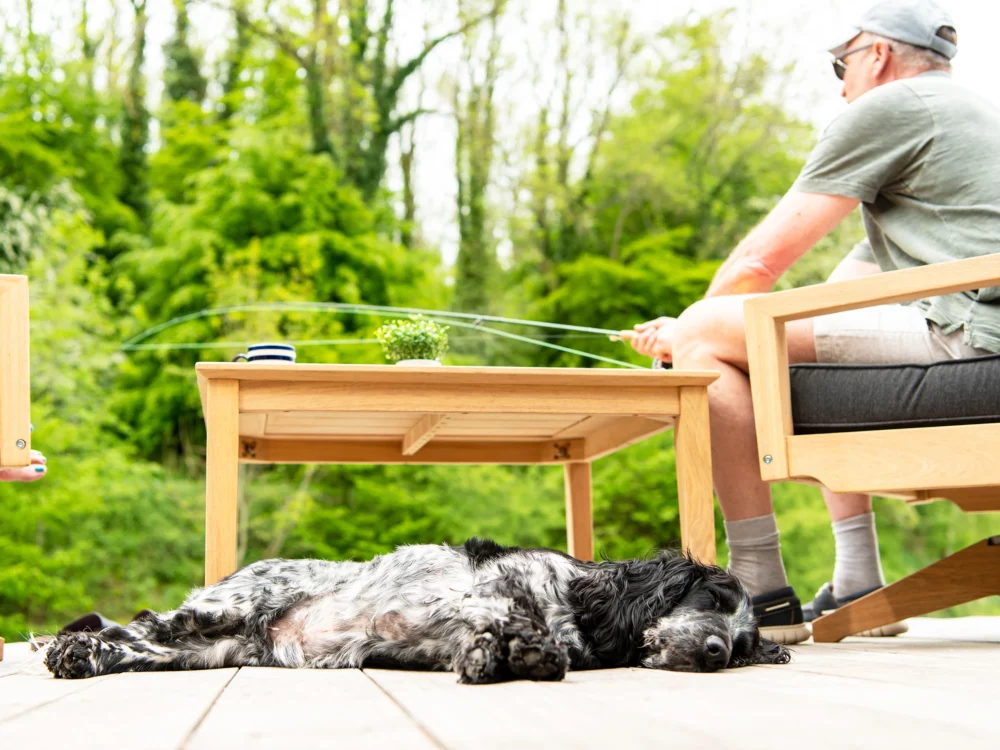 Alexander Rose Tivoli Roble Swivel Lounge Chair and Side table Man Fishing and Dog sleeping in the foreground High Quality Hardwood Garden Furniture